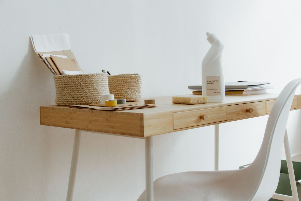 Un bureau à domicile propre et bien rangé, avec des produits de nettoyage, des papiers et des paniers de rangement.